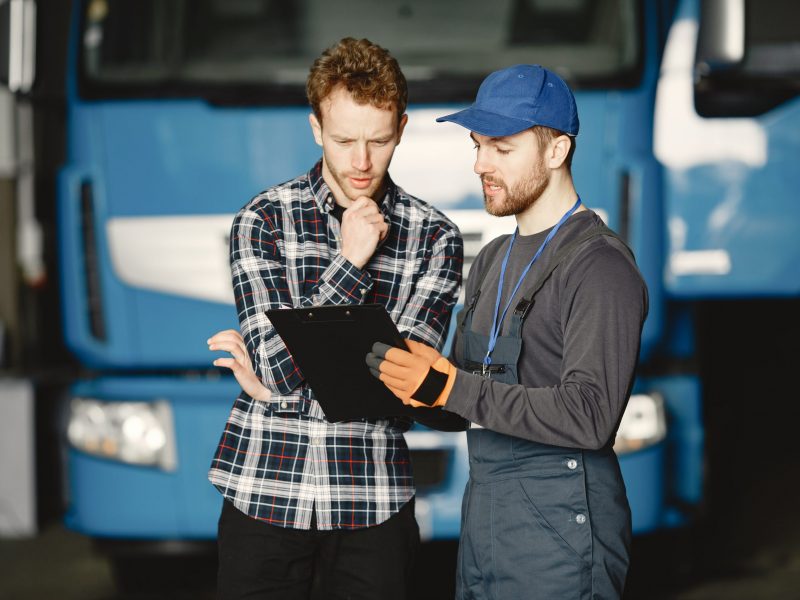 Two guys talking about work. Work in garage near truck. Transfer of documents with goods